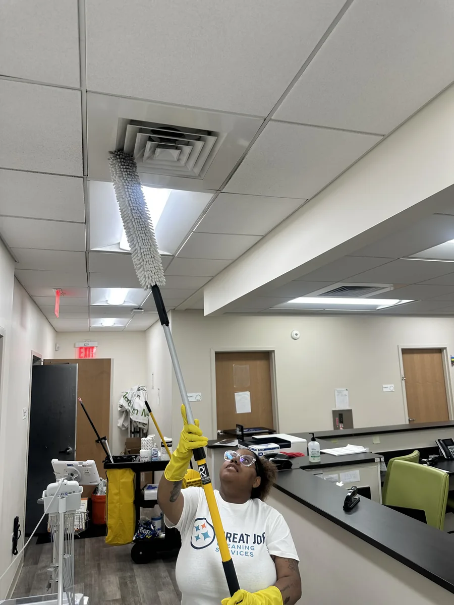 Great Job team member dusting a ceiling vent with an extension duster